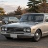 角張ったC10型の4ドアセダンを中心に、2ドア車とワゴン系車両が並ぶ郊外の情景